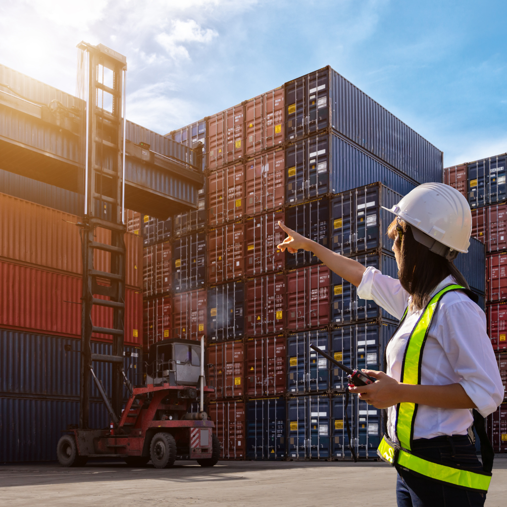 Woman standing in a supply chain 3PL yard guiding a reach stacker as it places an intermodal container.