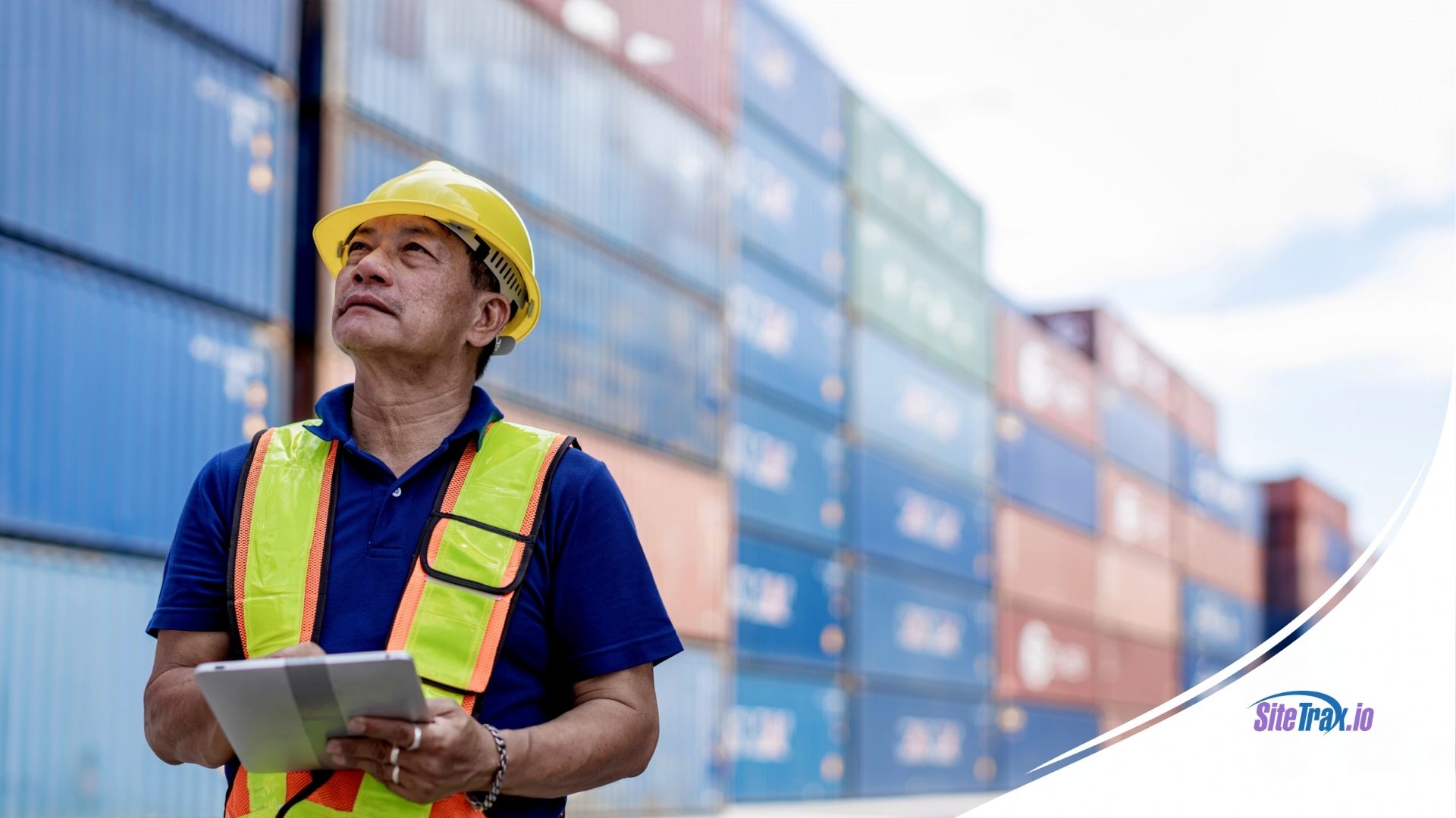 Port worker wearing a yellow hard hat and safety vest holds a tablet for their terminal operating system while inspecting stacked intermodal containers at a shipping yard. The SiteTrax.io logo is displayed in the bottom right corner.